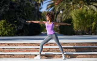 Black woman adopting warrior yoga pose outside on a bright sunny day